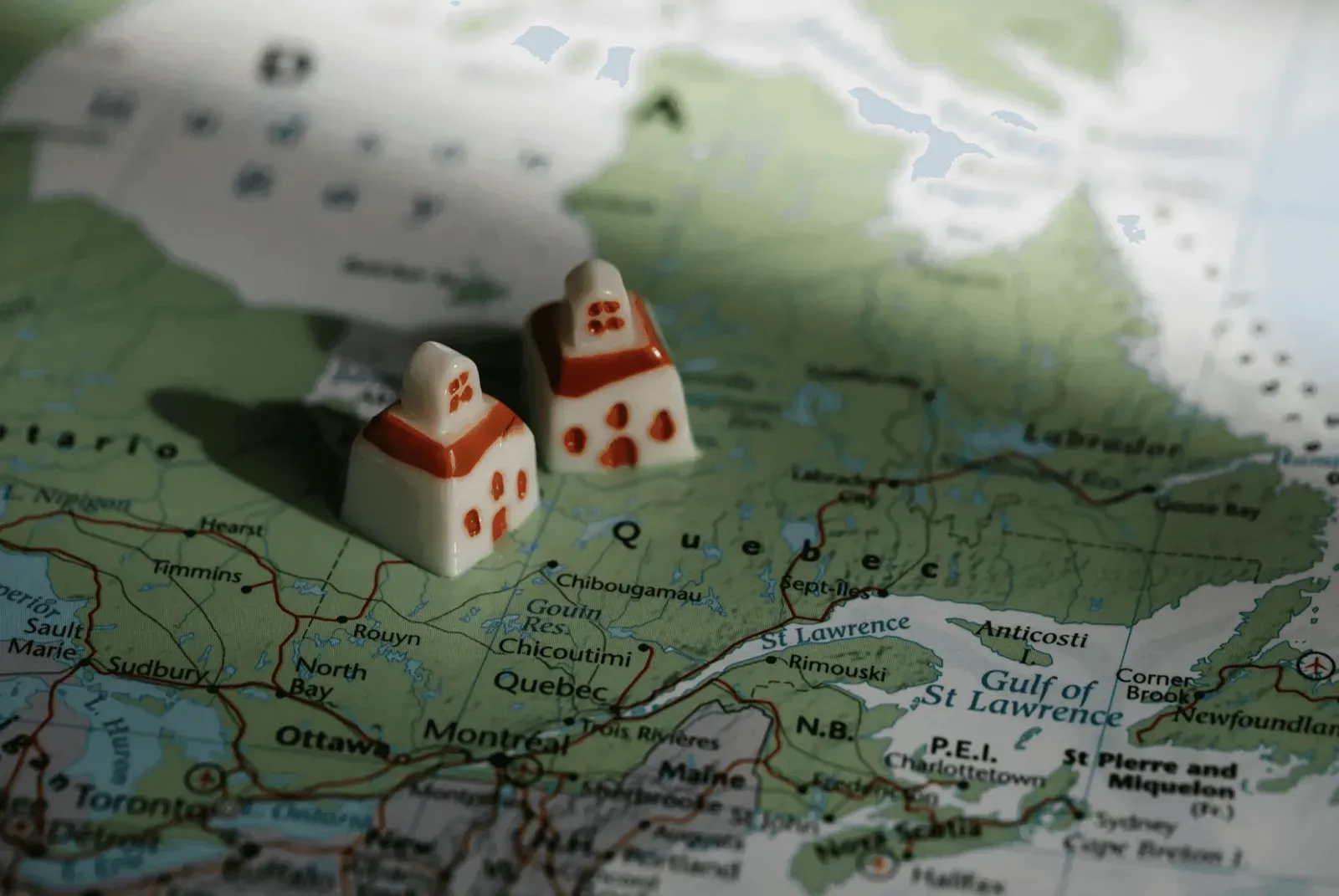 Two small white house tokens with red roofs sit on a map of Canada, showing Quebec and nearby provinces.