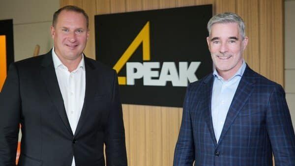 Two smiling men in business suits stand in front of a "4 PEAK" logo sign.