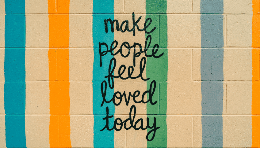 Colorful vertical stripes on a beige brick wall with black text: 'make people feel loved today'.