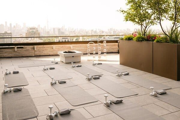 Rooftop yoga area with multiple mats, small weights, and a fire pit, overlooking a city skyline at sunset.