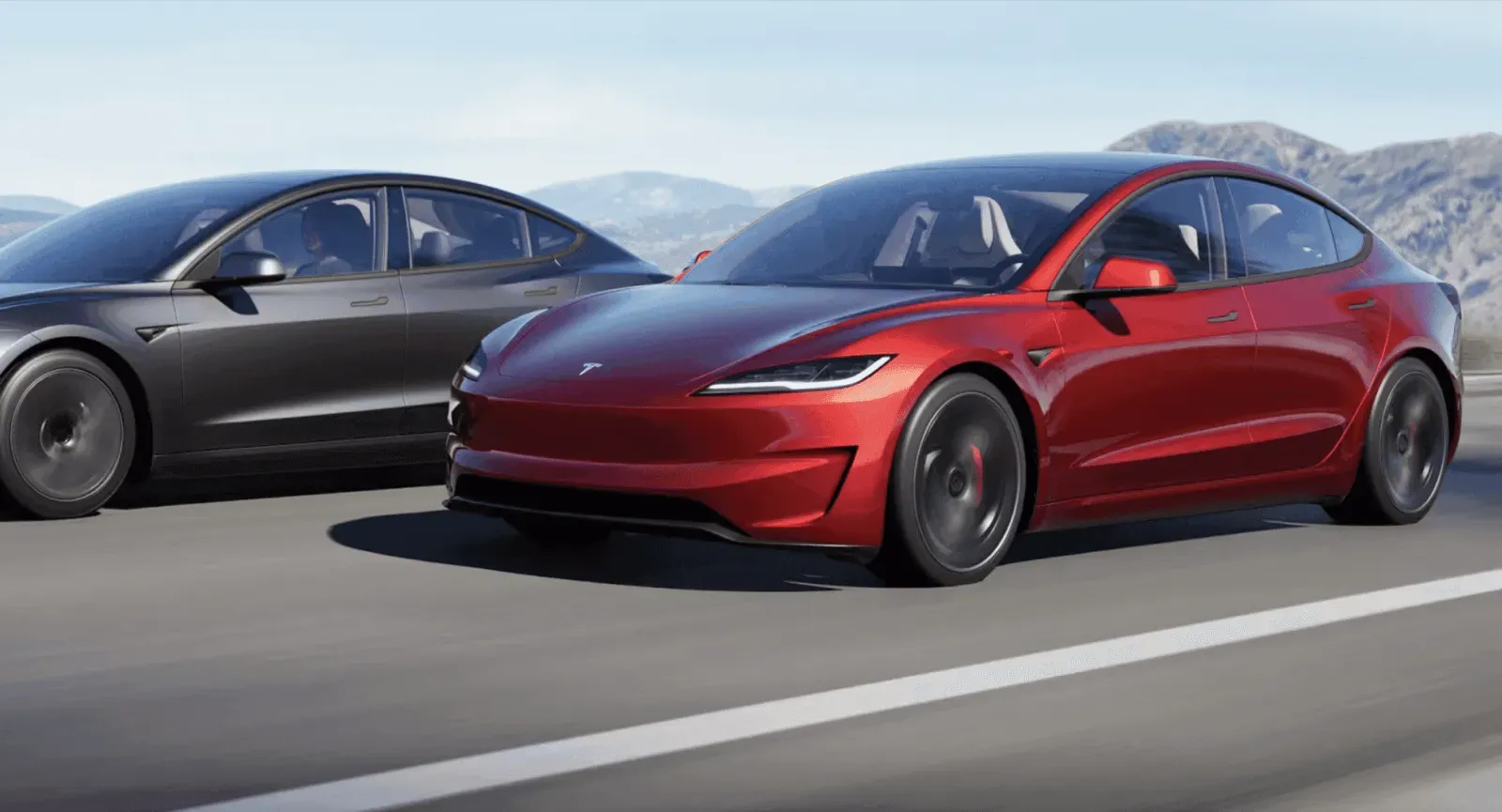 Sleek red Tesla Roadster and dark grey Tesla Model 3 driving on a highway, mountains in background.