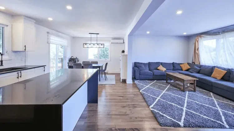 Modern open-concept home with a kitchen island, dining area, and living room featuring a blue sectional and patterned rug.