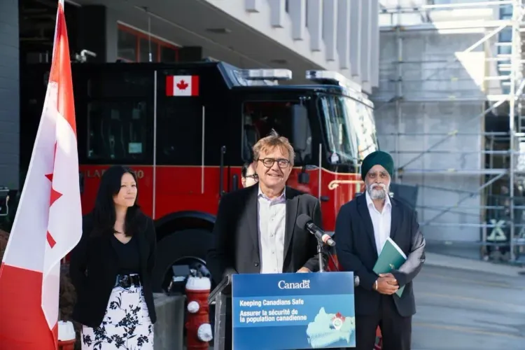 Three Canadian officials, including a man speaking at a podium, stand before a fire truck and Canadian flag.