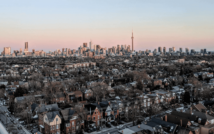 Aerial view of Toronto skyline with CN Tower behind residential houses and bare trees at sunrise/sunset.