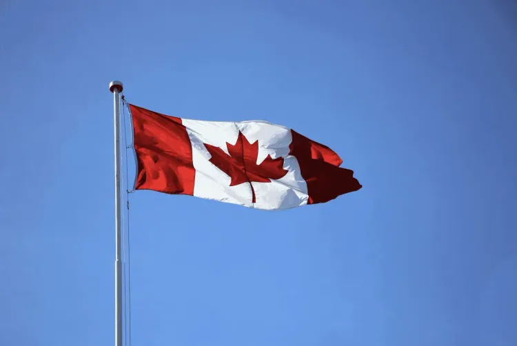 A Canadian flag, red and white with a maple leaf, waves on a flagpole against a clear blue sky.