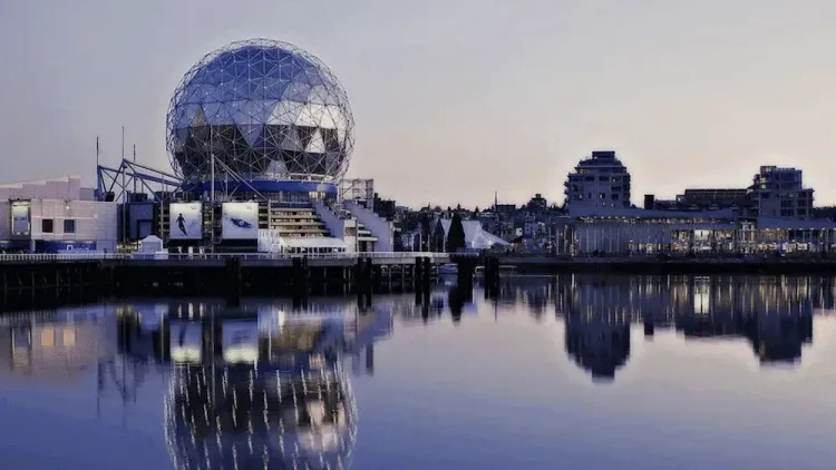 Vancouver's Science World geodesic dome and city skyline reflected in water at dusk.