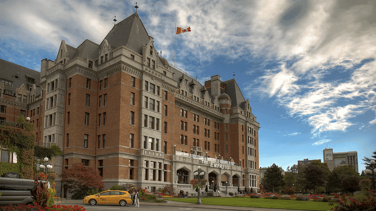 Grand Fairmont Empress Hotel in Victoria, BC. Chateauesque architecture with red brick, grey roofs, gardens, taxi.