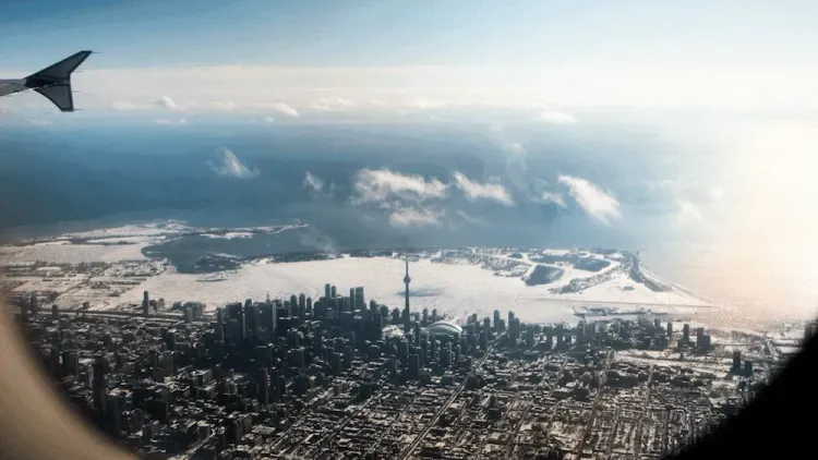 Aerial view of snowy Toronto, including CN Tower, Rogers Centre, and frozen Lake Ontario, from an airplane window.