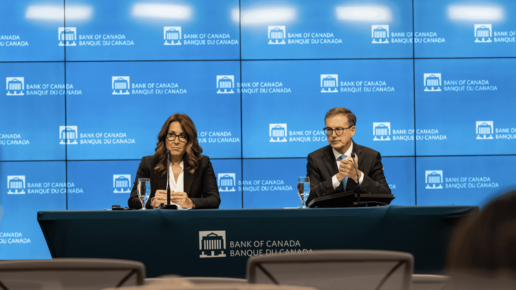 Two speakers sit at a Bank of Canada press conference table with microphones.
