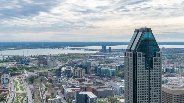 Elevated view of Montreal city, featuring a unique glass skyscraper, river with bridges, and urban landscape.