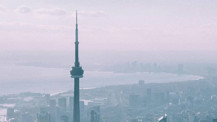 CN Tower stands tall over a hazy Toronto cityscape and Lake Ontario.