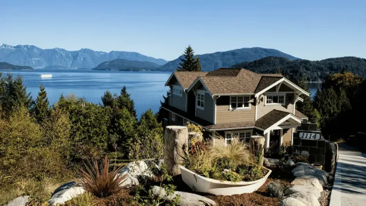 Waterfront house with a boat planter overlooking a bay with mountains and a ferry.