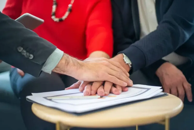 Three hands stacked on business documents on a table, symbolizing agreement or collaboration.