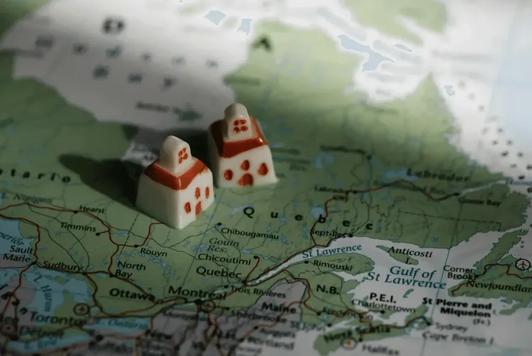 Two small white house tokens with red roofs sit on a map of Canada, showing Quebec and nearby provinces.