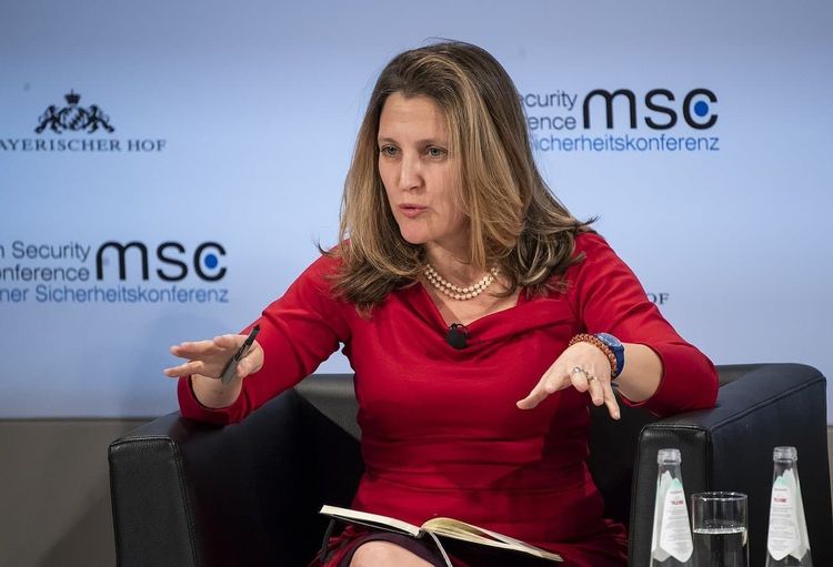 Chrystia Freeland in a red dress speaks at the Munich Security Conference, gesturing with her hands.
