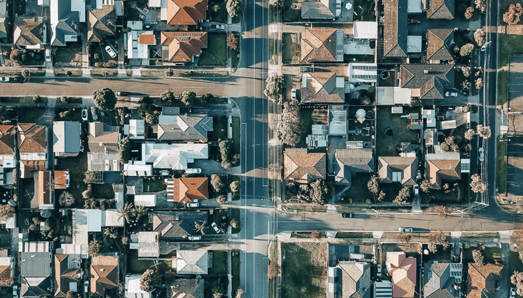 Aerial view of a suburban neighborhood with many houses, intersecting streets, and scattered trees.