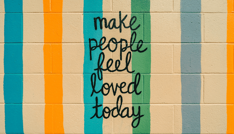 Colorful vertical stripes on a beige brick wall with black text: 'make people feel loved today'.