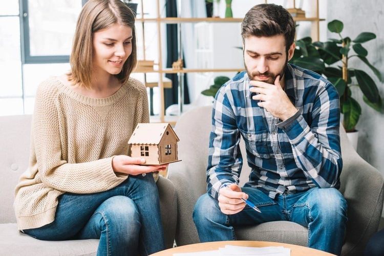 Woman holding a miniature house, man with a pen, contemplating homeownership.