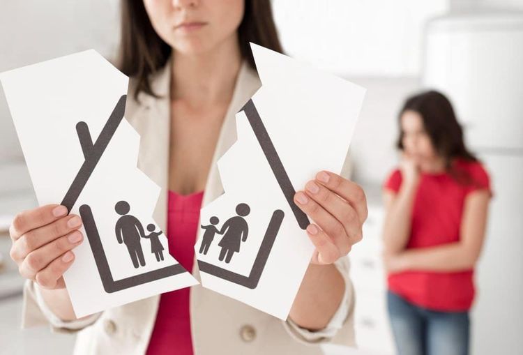 Woman holds torn paper showing a family icon split in two (father/child, mother/child), with a sad child blurred in background.