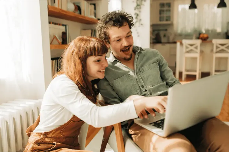 Smiling woman in brown overalls points at a laptop with a surprised man.