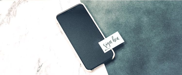 A smartphone with a 'Sign here' note pointing to its screen, on a marble and dark textured background.