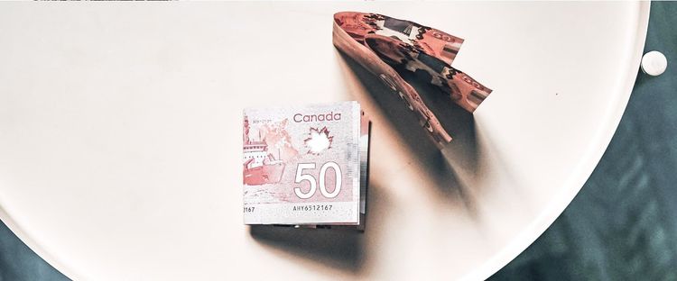 A stack of Canadian $50 bills next to several folded ones on a light surface.