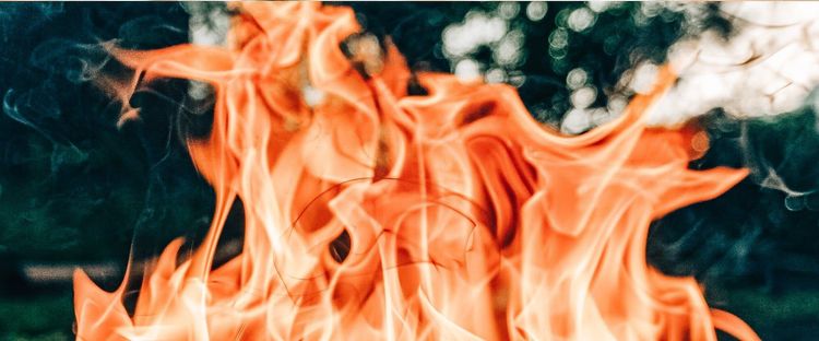 Vivid orange flames with dark smoke against a blurred green background.