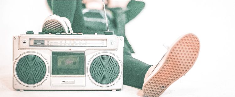 Vintage white boombox with a cassette tape. A person in sneakers relaxes with legs outstretched.
