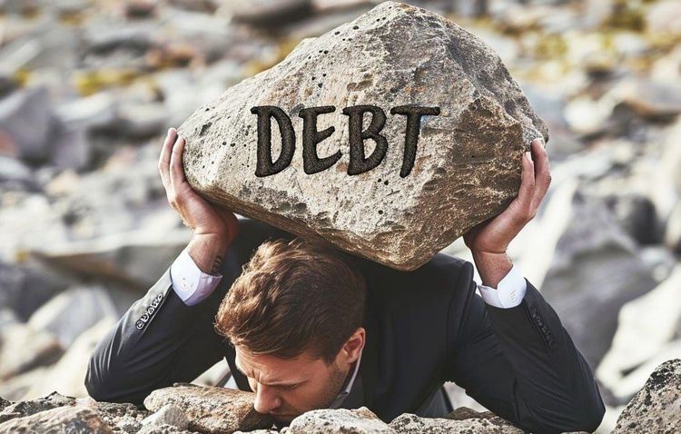 Businessman struggles, hunched under a large rock labeled "DEBT", illustrating financial burden.