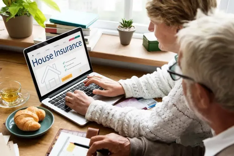 Two older adults reviewing "House Insurance" on a laptop; one types, the other takes notes.