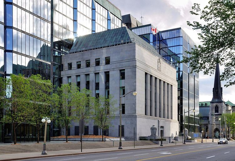 Bank of Canada building: grey stone with a green roof, alongside modern glass high-rises, trees, and a church steeple.