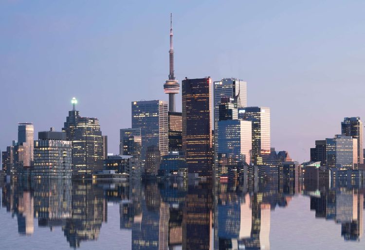 Toronto skyline at dusk with the CN Tower and buildings reflected in still water.