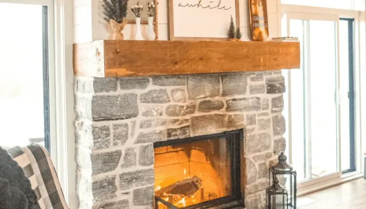 Stone fireplace with a warm fire, wooden mantel, and cozy decor in a bright living room.