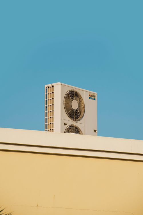 White Mitsubishi Electric AC unit with two fans on a beige building roof under a clear blue sky.