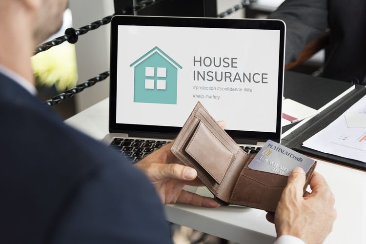 A person holds a wallet with a credit card, viewing "HOUSE INSURANCE" on a laptop screen.