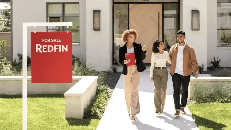Redfin agent shows a house with a 'For Sale' sign to a happy couple.