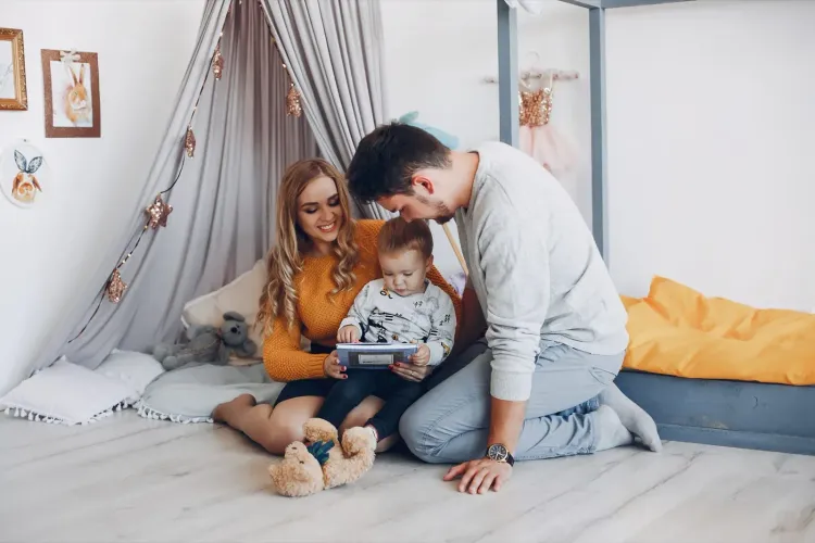 Happy family with toddler looking at a book on the floor in a bright, cozy bedroom.