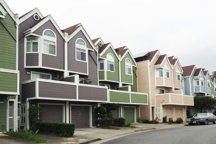 A curving row of colorful, multi-story townhouses with gabled roofs and garages, a car parked on the street.