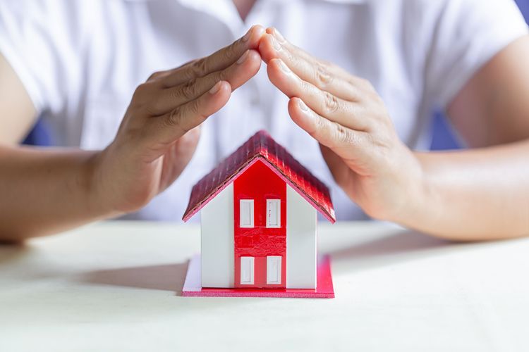 Hands cupped protectively over a small white house with a red roof and red window accents.