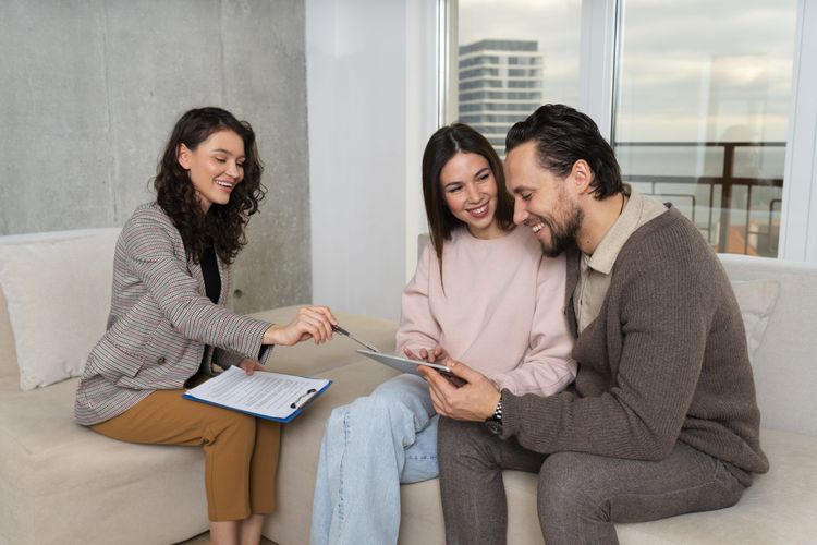 Smiling professional points pen at tablet with a happy couple on a couch.