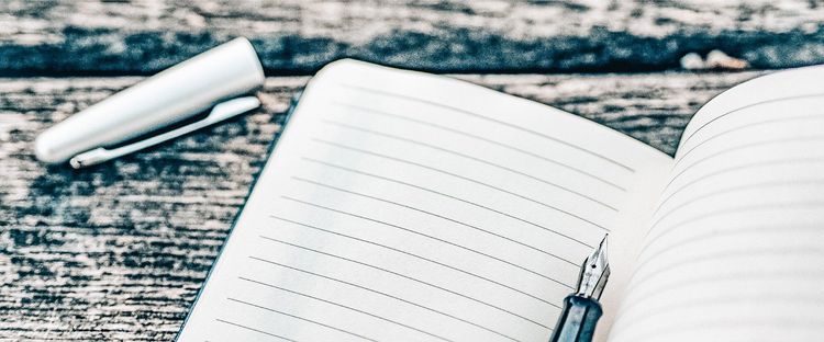 Open lined notebook with a fountain pen and its silver cap on a textured wooden surface.