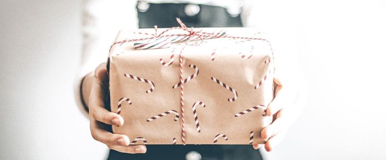 Hands hold a brown paper gift with red candy cane patterns and red-and-white striped twine.