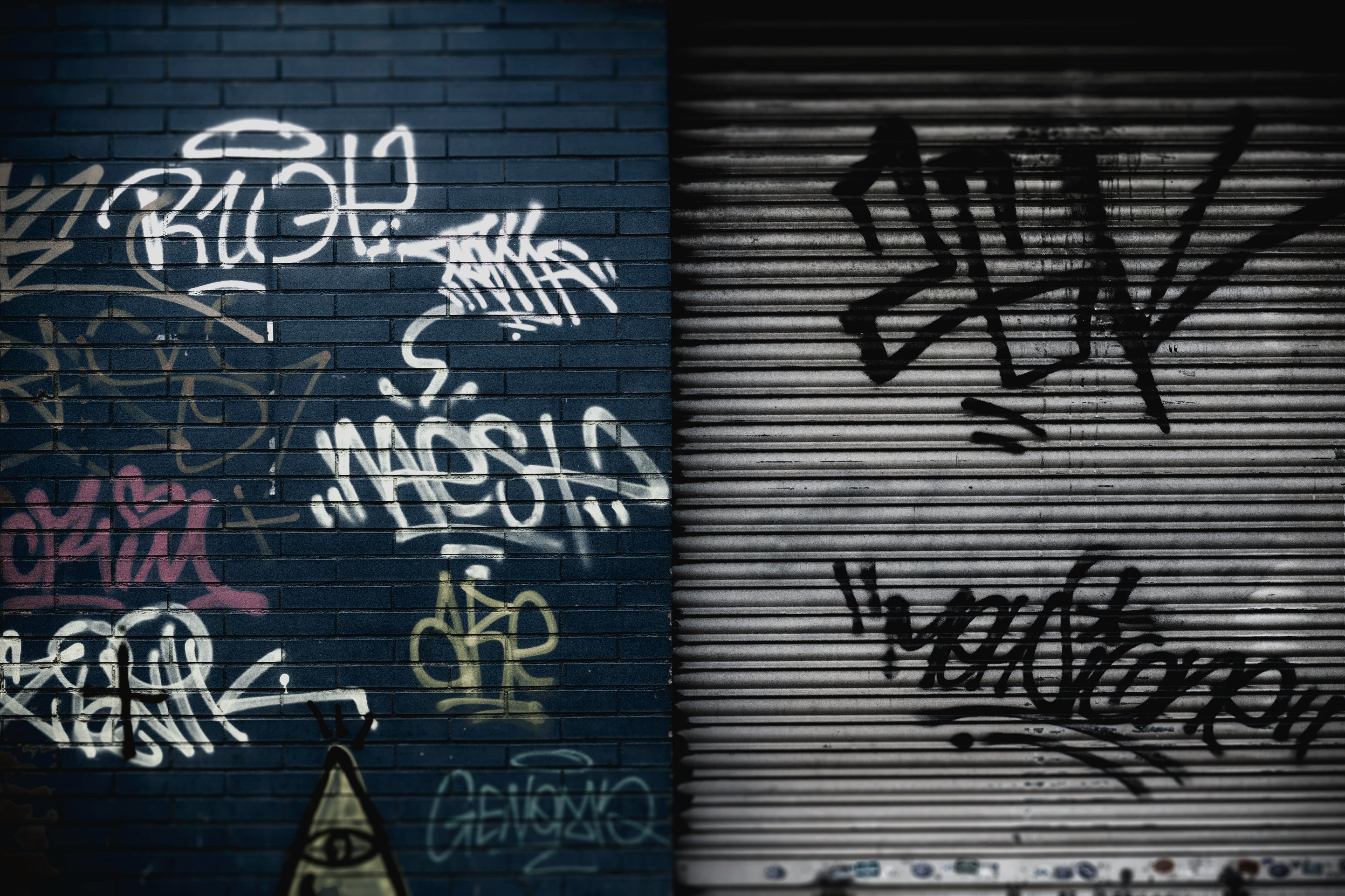 Dark blue brick wall with white graffiti on the left; gray metal shutter with black graffiti on the right.